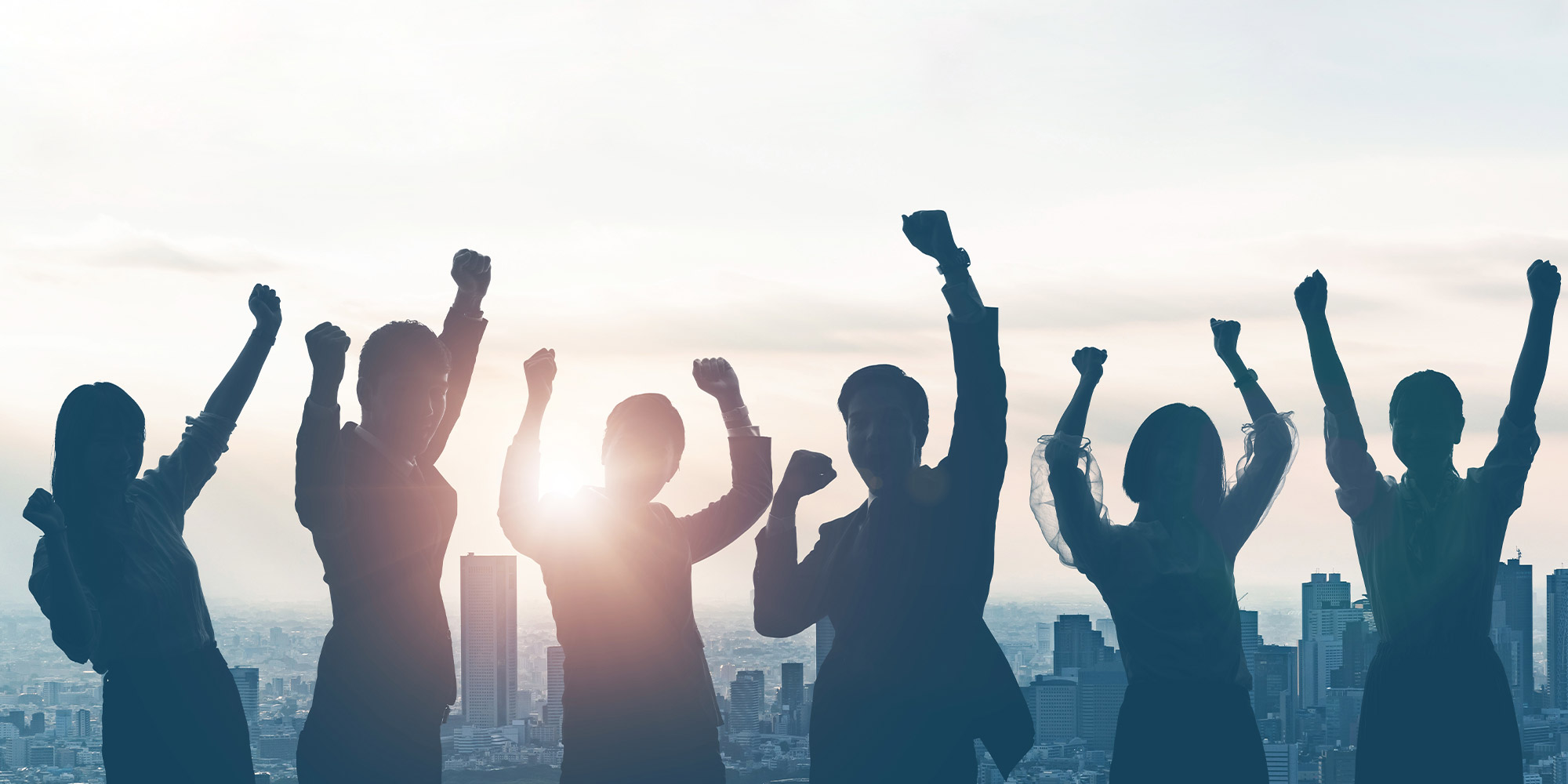 silhouette of six business people, standing in front of a sunset with their arms up in celebration