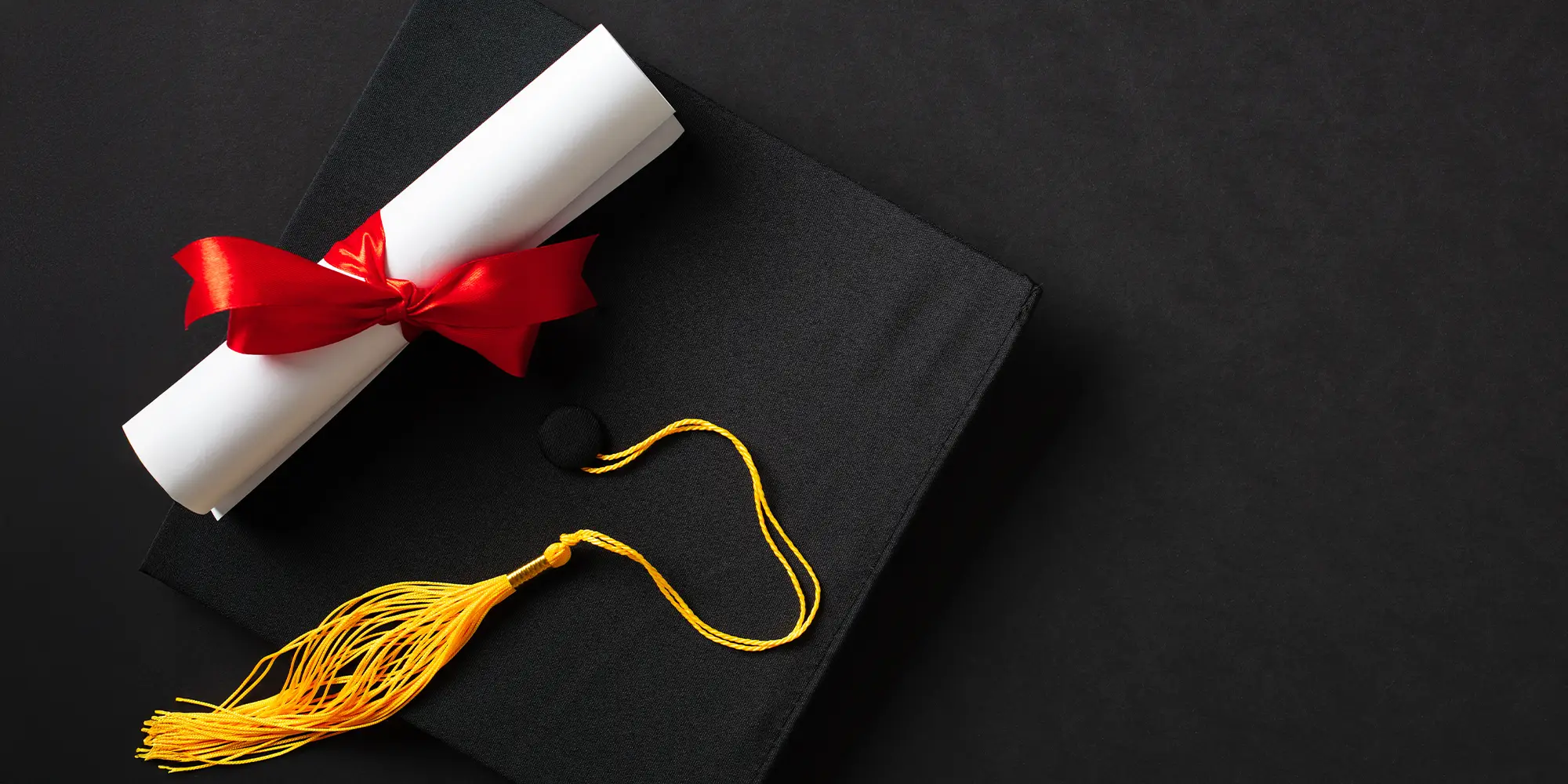 Graduation cap with a rolled diploma tied with a red ribbon