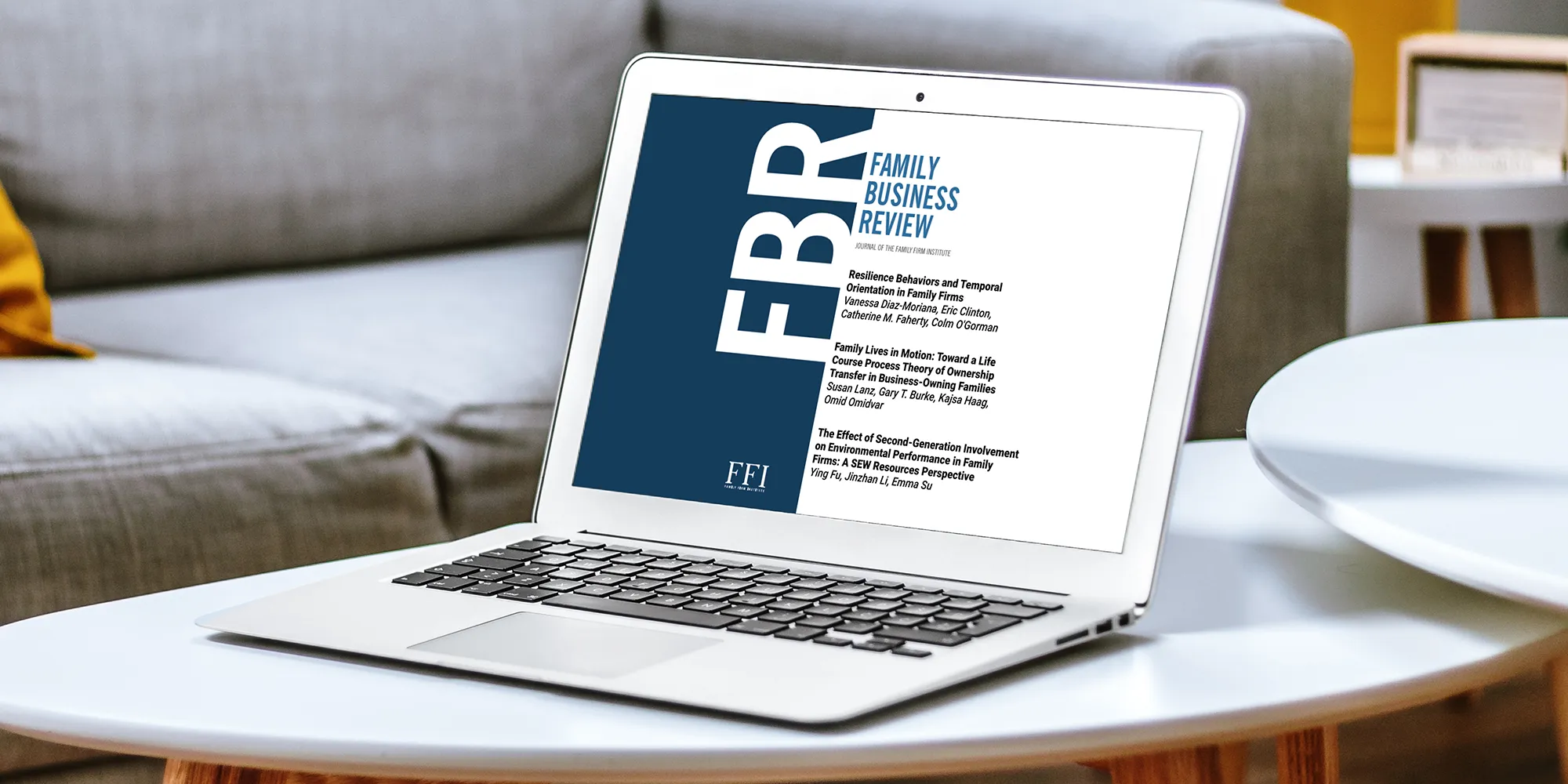 Laptop on a white coffee table displaying the 'Family Business Review' cover with titles of articles, representing business research and publications.