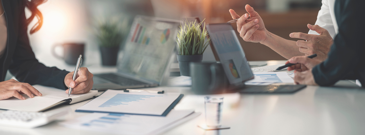 Office desk with laptops, papers with charts, and two people collaborating.