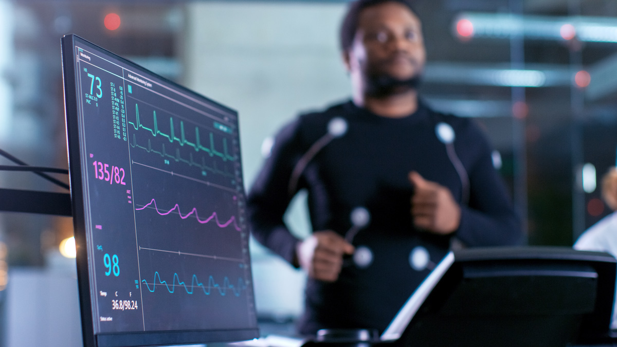 A health monitor displaying vital signs next to a person jogging on a treadmill with sensors attached to their body.