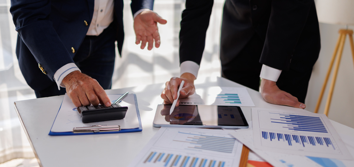 Two business people point to graphs and charts to analyze market data, balance sheet, account, net profit to plan new sales strategies to increase production capacity