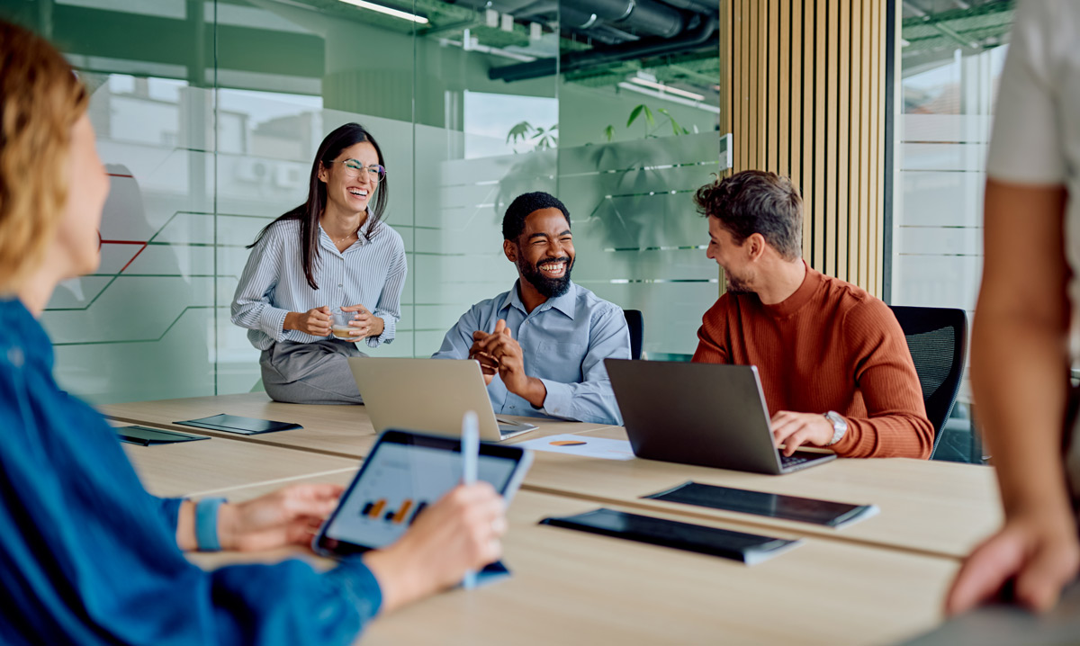 A group of cheerful professionals laughs during a meeting in a glass-walled conference room, creating a positive and collaborative atmosphere.