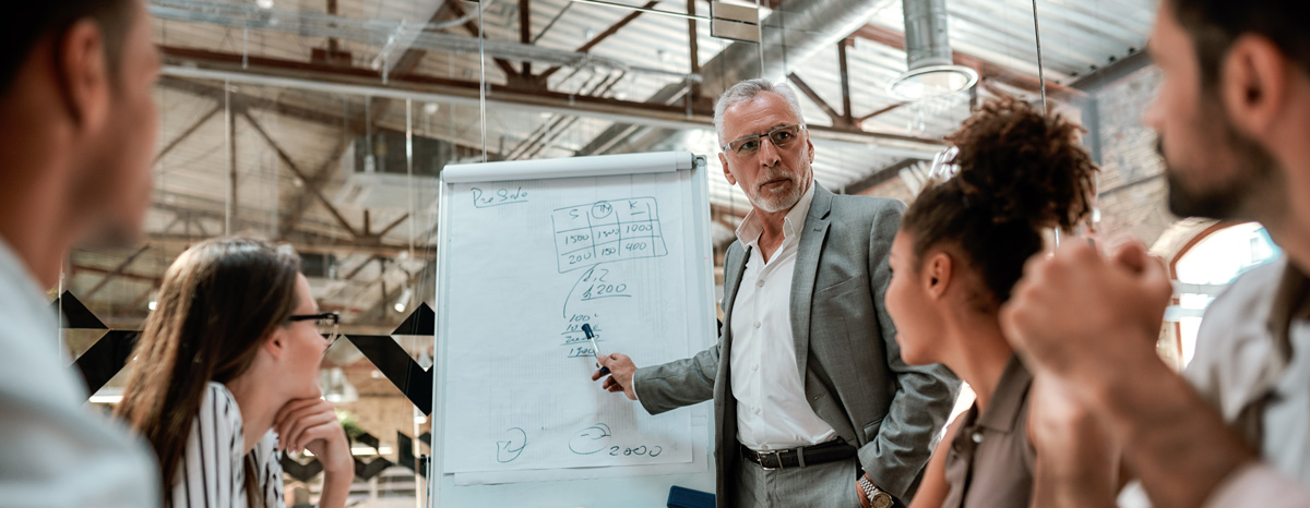 A group of people in a modern office, discussing a presentation on a flip chart.