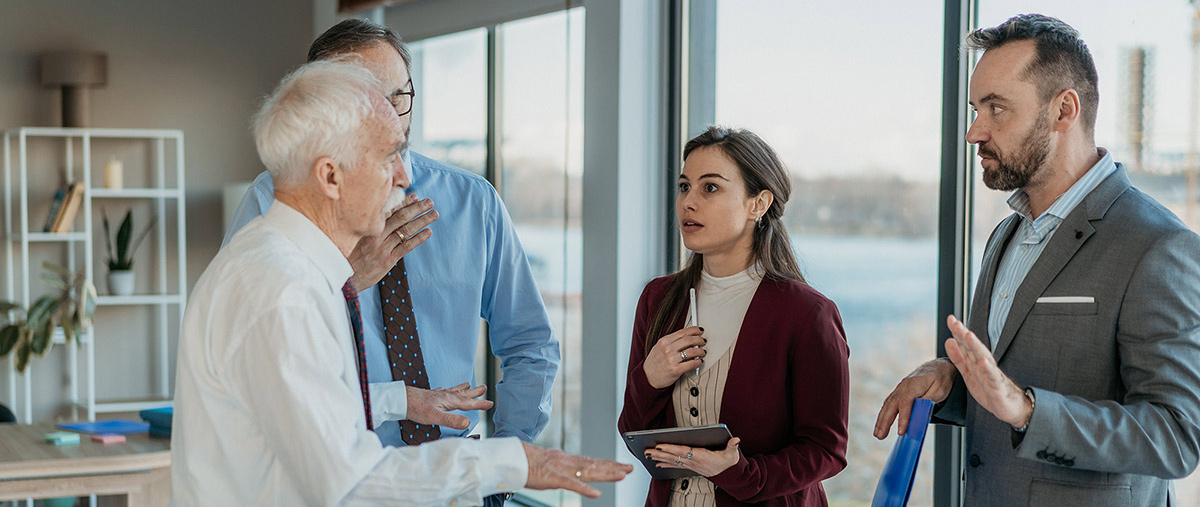 Four family members engaged in a serious discussion or debate near a window in a bright office environment.