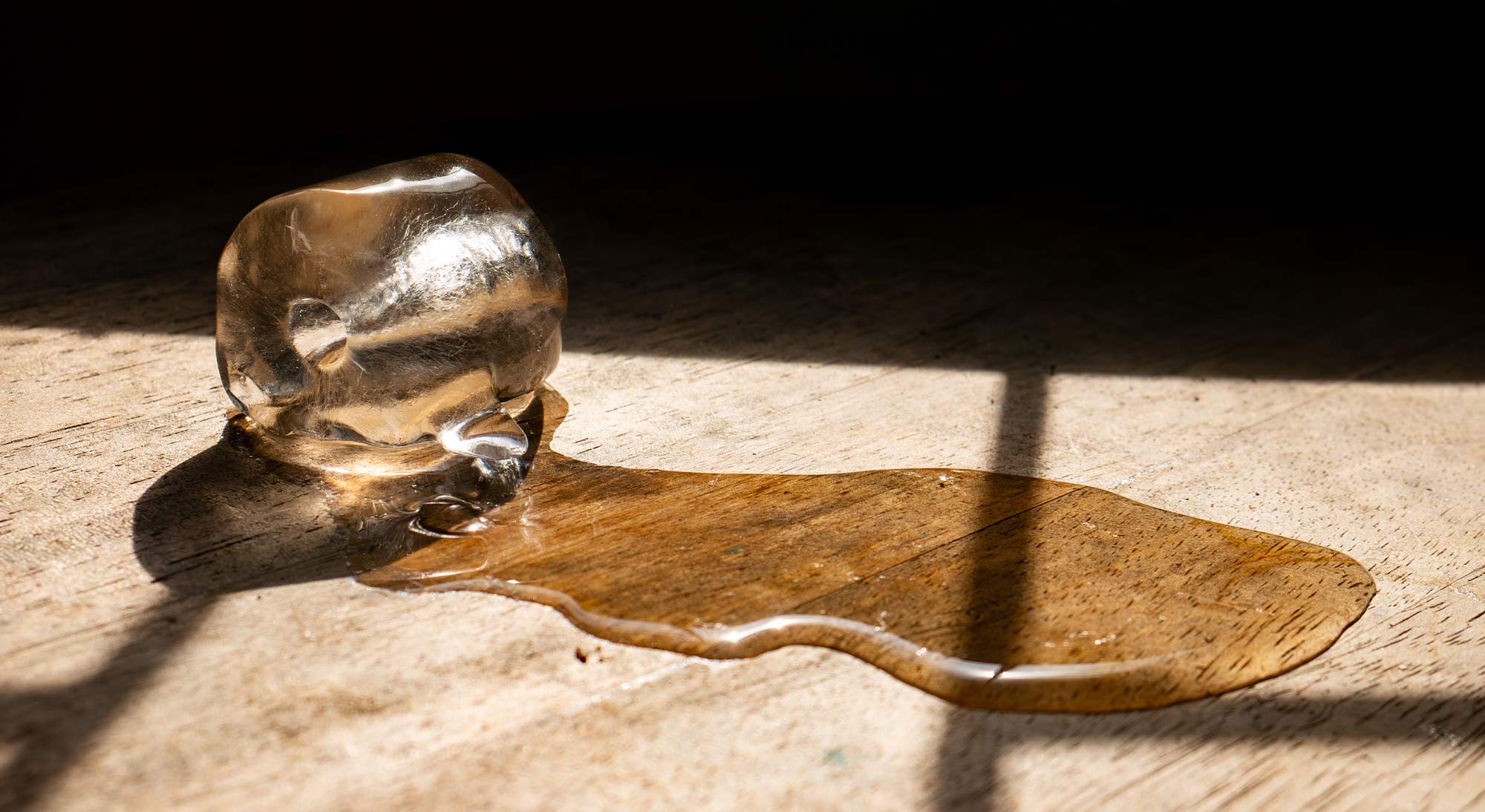 An ice cube melting on a wooden counter against a black background