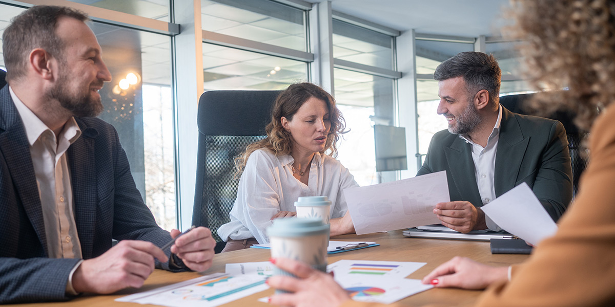 Colleagues reviewing printed charts and holding coffee cups during a meeting.