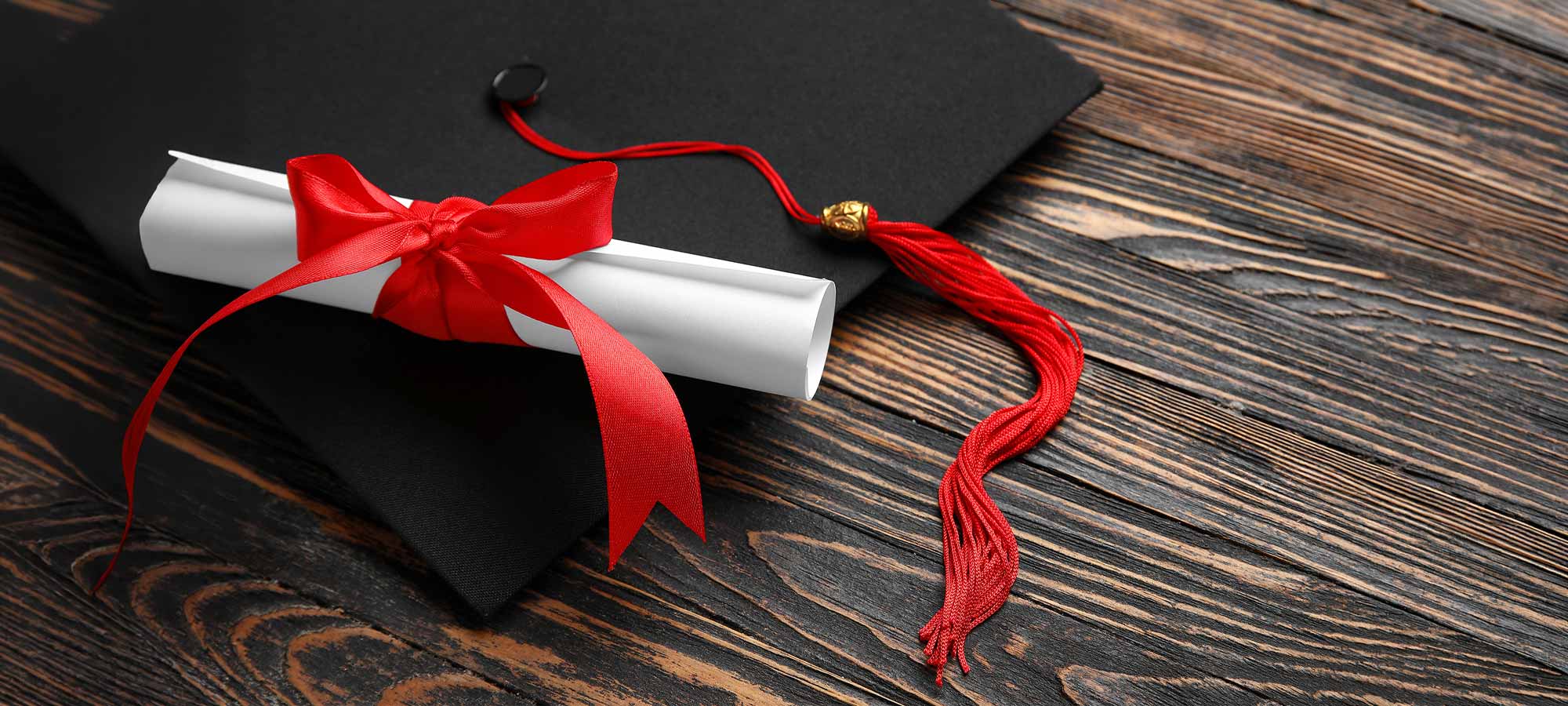 Black graduation cap with a red tassel alongside a scroll tied with red ribbon.